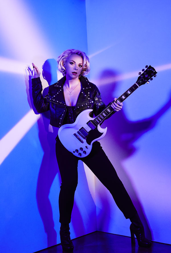 Samantha Fish with guitar against purple wall backdrop