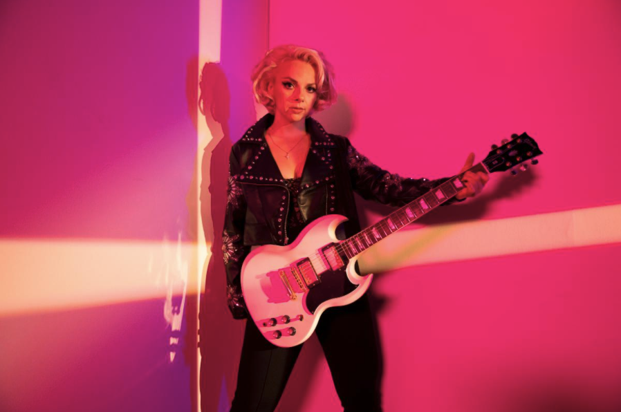 Samantha Fish with guitar against red wall backdrop
